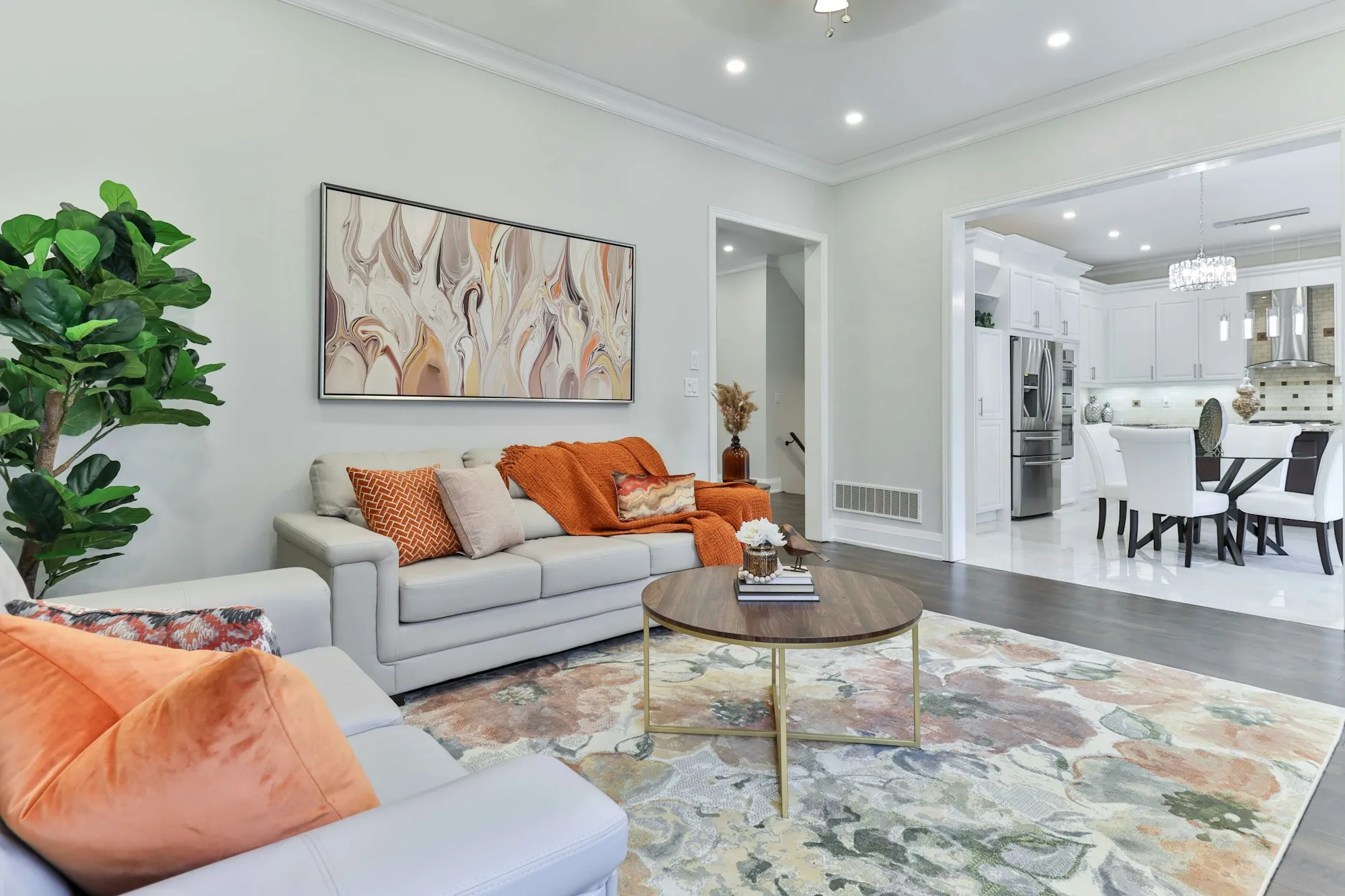 Open living room with an orange-accented sofa and a white kitchen